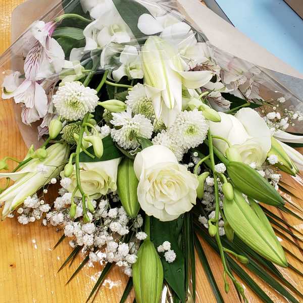 Wrapped bouquet of white roses, lilies, and chrysanthemums with a sheer bow on a wooden table