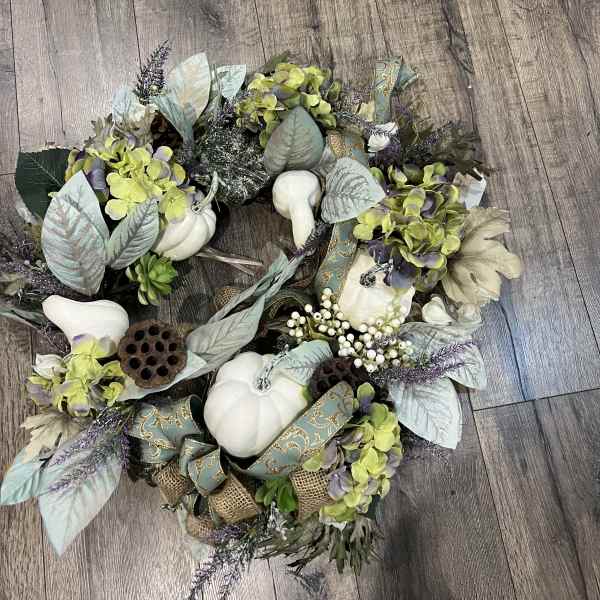 Decorative wreath with white pumpkins, hydrangeas, and ribbon on a wood floor