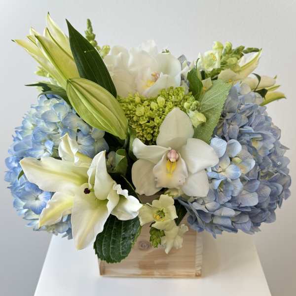 Blue hydrangeas and white orchids arranged in a wooden box