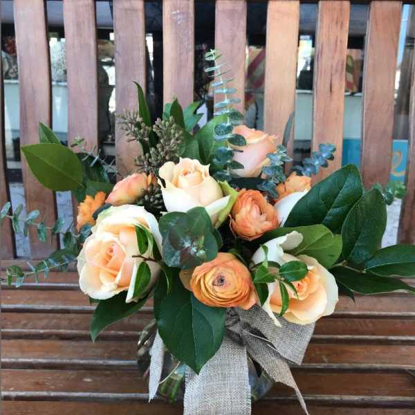 Peach roses and orange blooms arranged in a clear glass vase with a burlap bow