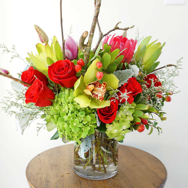 Mixed arrangement of red roses, green hydrangeas, orchids and protea in a clear glass cylinder vase