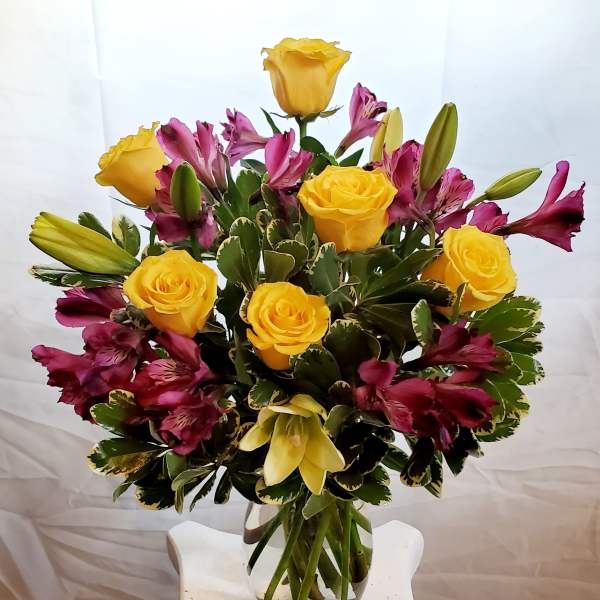 Yellow roses and magenta lilies arranged in a glass vase