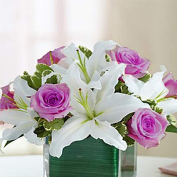 White lilies and pink roses arranged in a clear square vase