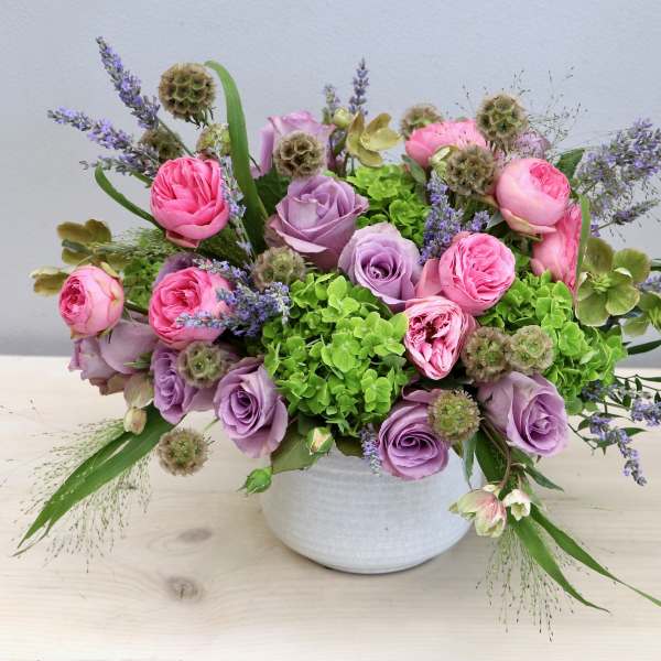 Low arrangement of pink and lavender roses with green hydrangeas in a white bowl vase