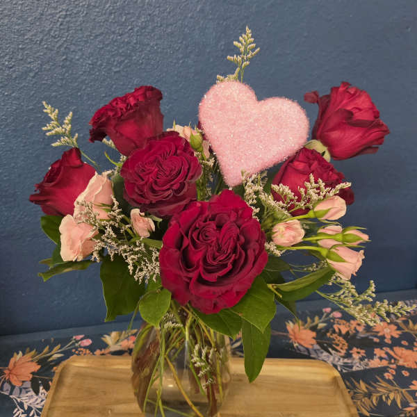 Red and blush roses in a glass vase with a pink heart pick