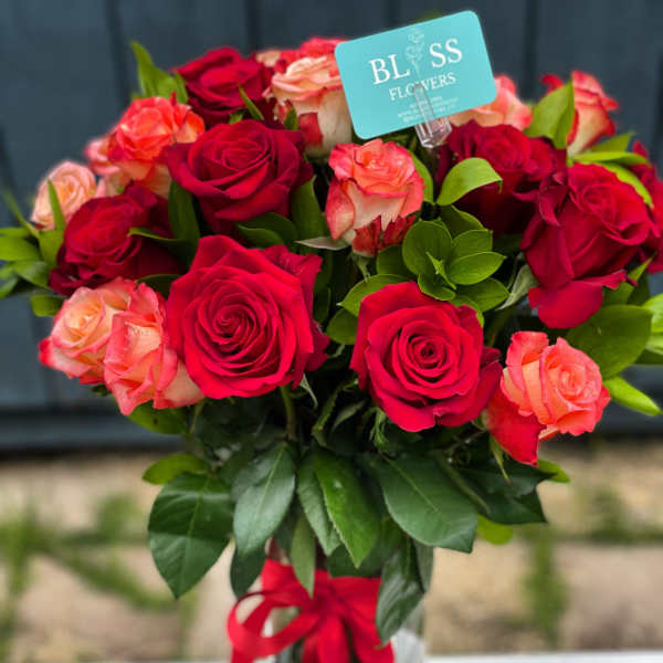 Bouquet of red and peach roses in a glass vase with a red ribbon