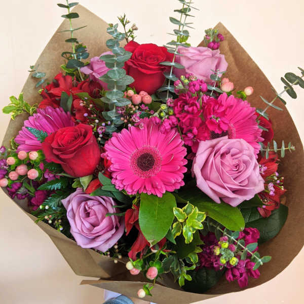 Bouquet of pink and red roses with gerbera daisies in brown paper
