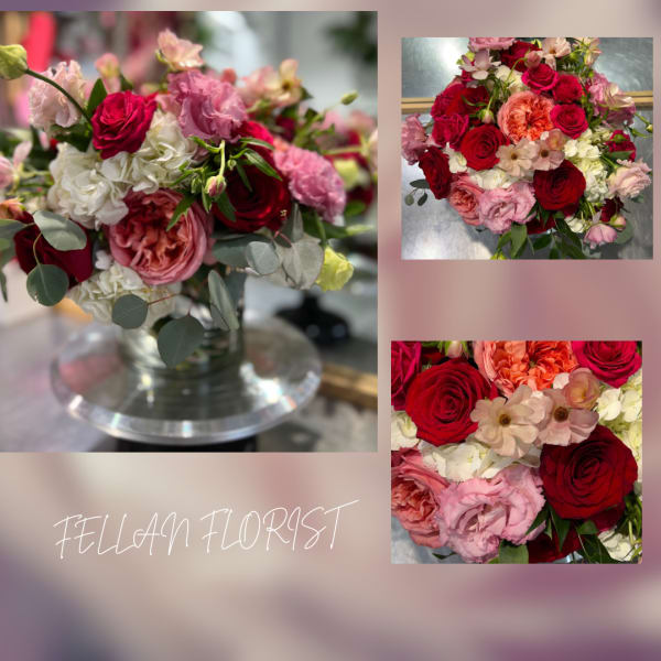 Low arrangement of red and pink roses with white blooms in a clear glass vase on a pedestal stand