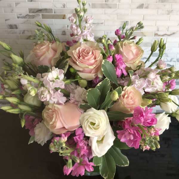 Rounded arrangement of blush roses, white blooms, and pink flowers in a glass vase