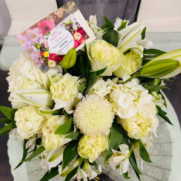 White bouquet of roses, lilies, and chrysanthemums with a florist card