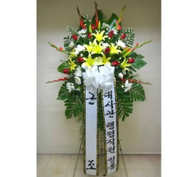 Tall standing spray with yellow lilies, red roses, white flowers, and long message ribbons in Korean.