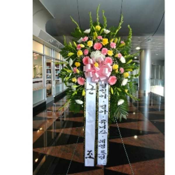 Tall standing spray of pink, yellow, and white flowers with a large pink bow and Korean message ribbons