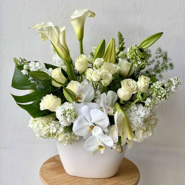 White floral arrangement in a white vase with calla lilies, roses, and orchids
