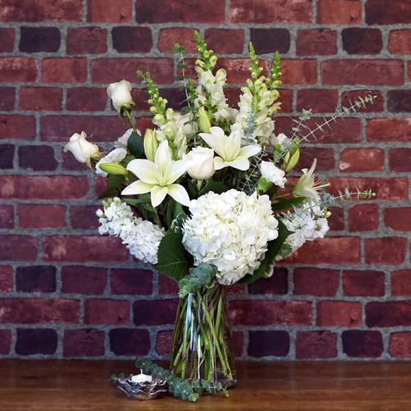 Tall arrangement of white lilies, roses, and hydrangeas in a clear glass vase