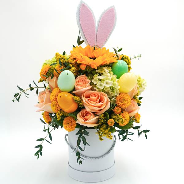 Bouquet of peach roses and orange flowers in a white hatbox with pastel bunny ears