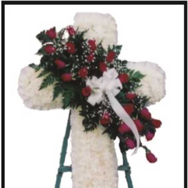 White floral cross on a stand with red roses and a white ribbon