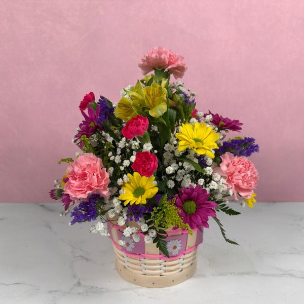 Basket of mixed pink carnations, yellow and purple daisies, and white filler flowers.