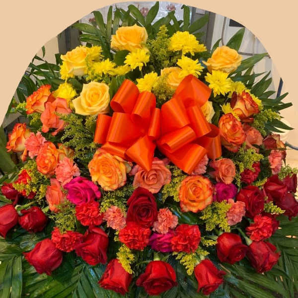 Large floral spray of red, orange, and yellow roses with a bright ribbon bow