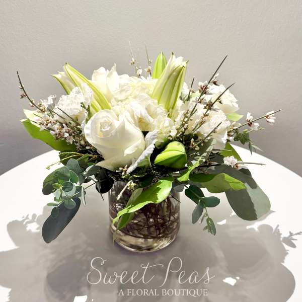 White roses and lilies arranged in a clear glass vase with greenery