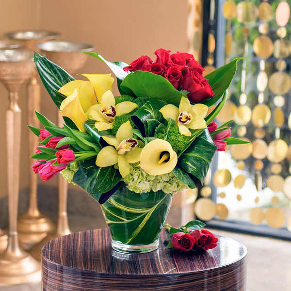 Bouquet of red roses, yellow orchids, and pink tulips in a glass vase