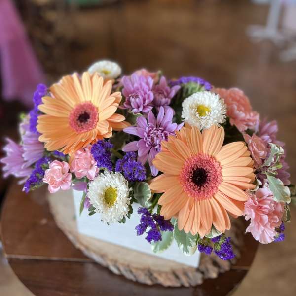 Bouquet of peach gerbera daisies, pink carnations, and purple flowers in a white box