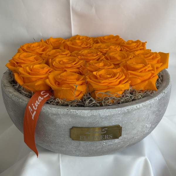 Orange roses arranged in a round silver bowl with an orange ribbon