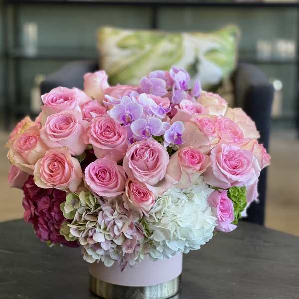 Pink roses and hydrangeas with purple orchids in a round box arrangement