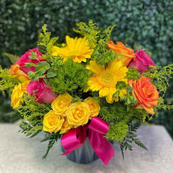 Bouquet of yellow daisies and pink-orange roses in a vase with a magenta ribbon