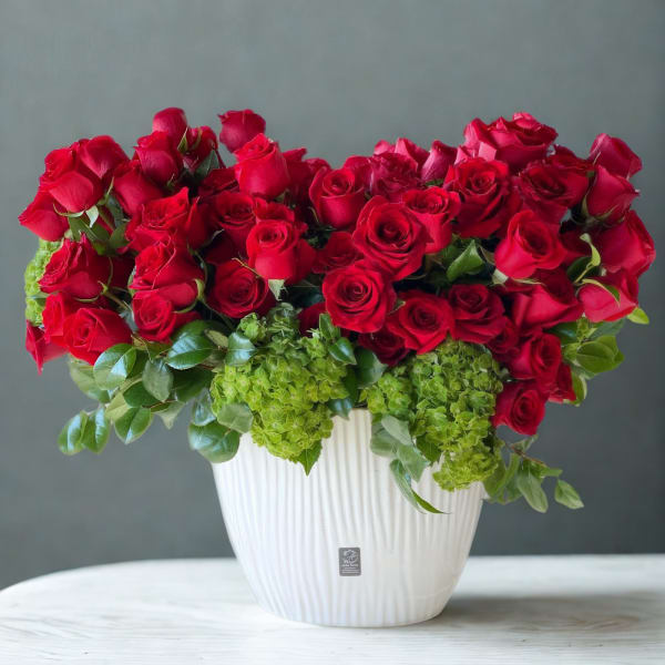 Red roses arranged in a white vase with green hydrangeas
