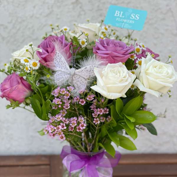 Bouquet of pink and white roses in a glass vase with a purple ribbon