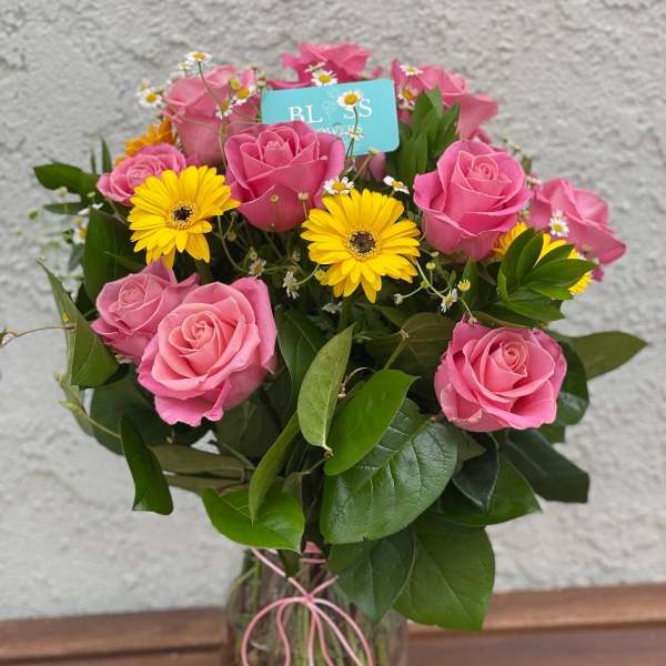 Pink roses and yellow daisies in a clear glass vase