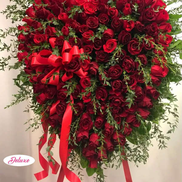 Heart-shaped red rose arrangement with red ribbon and greenery
