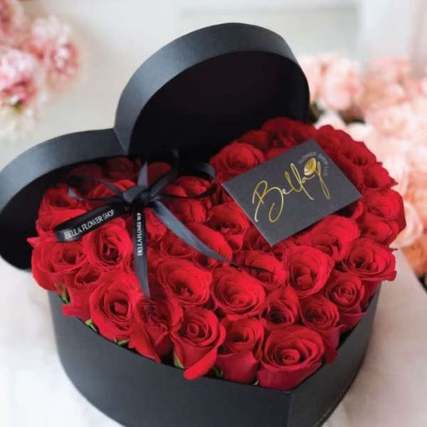 Heart-shaped box filled with red roses and tied with a black ribbon
