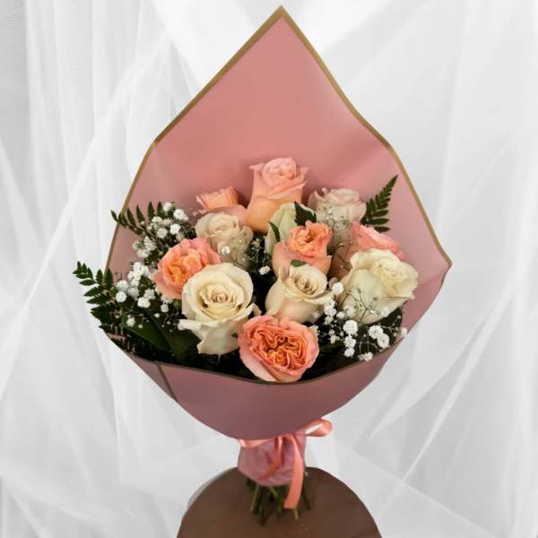 Bouquet of peach and cream roses with white filler flowers wrapped in pink paper