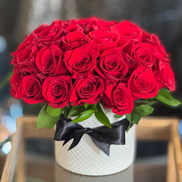 Red roses arranged in a white hatbox with a black ribbon