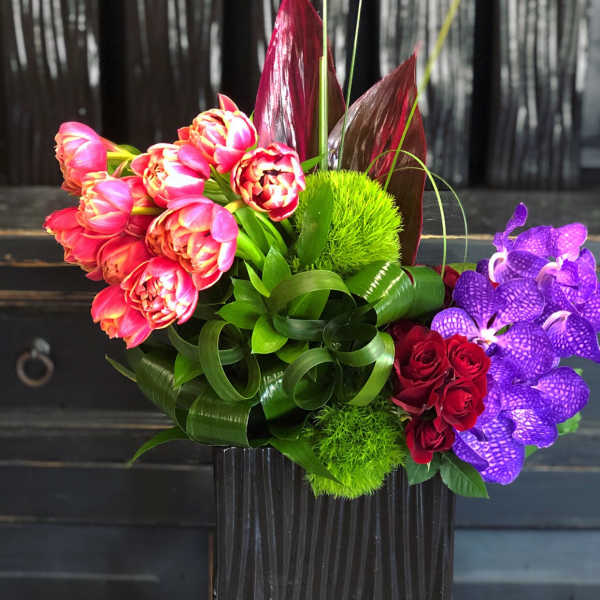Colorful bouquet with tulips, roses, and purple orchids in a black vase