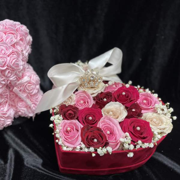 Pink rose teddy bear beside a heart-shaped rose box with a ribbon