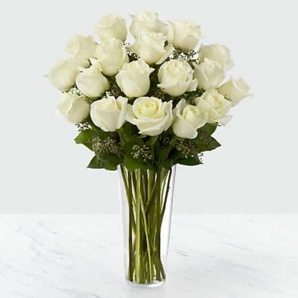 Tall clear vase of long-stem white roses arranged in a rounded cluster