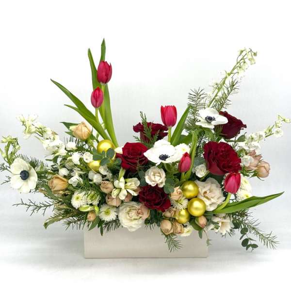 Low red and white floral arrangement with tulips, roses, anemones and gold ornaments in a white rectangular container