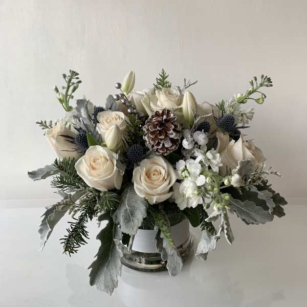 Cream roses and white lilies arranged in a glass vase with pinecone accents