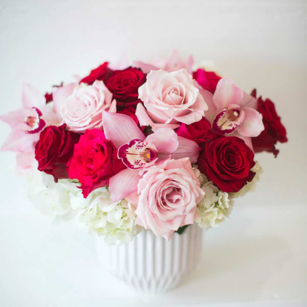 Pink and red roses with orchids in a white vase