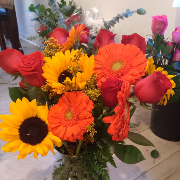 Mixed bouquet of sunflowers, gerbera daisies, and red roses in a glass vase