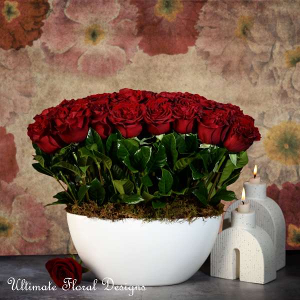 Red roses arranged in a white bowl with candles beside it