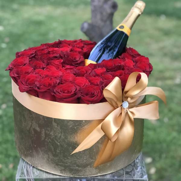 Red roses arranged in a round box with a champagne bottle and gold ribbon