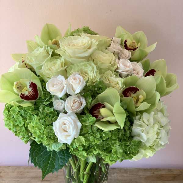 Bouquet of pale roses, green orchids, and hydrangeas in a glass vase