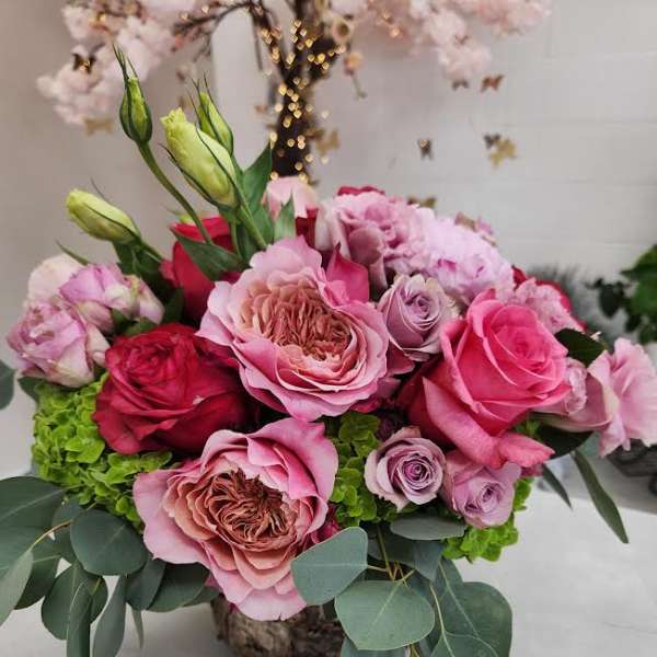Low arrangement of pink and red roses with green hydrangea in a rustic container