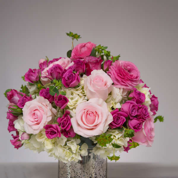 Round arrangement of light and hot pink roses with white hydrangeas in a silver cylinder vase