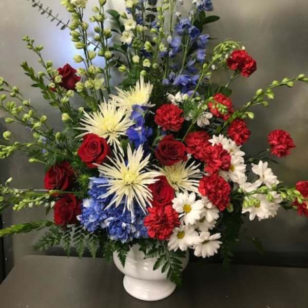 Tall mixed flower arrangement in a white vase with red, white, and blue blooms