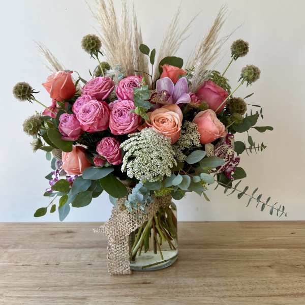 Pink and peach rose bouquet in a glass vase with dried grasses
