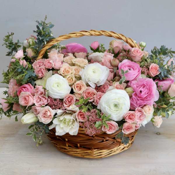 Low basket arrangement of pink and white roses and ranunculus in a woven wicker basket